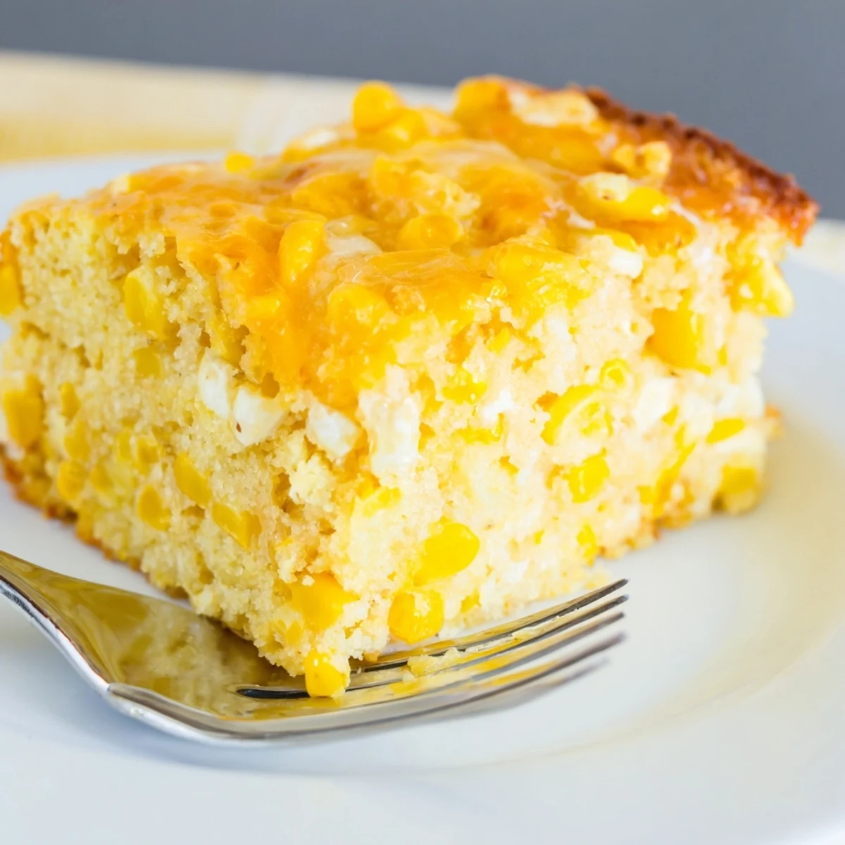 Warm classic Jiffy corn casserole scooped onto a white plate alongside roasted holiday meats