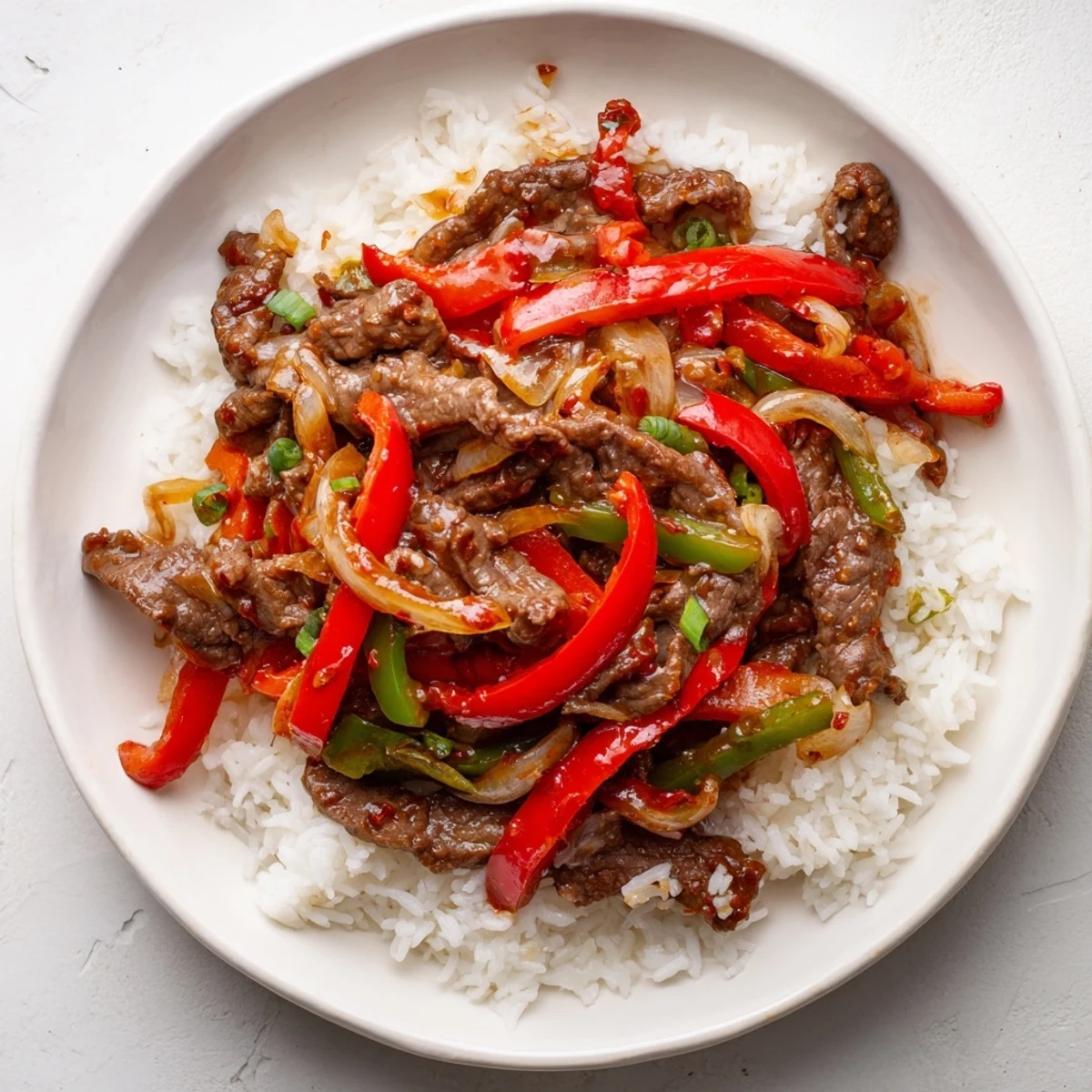 Close-up of spicy beef stir fry with chili garlic featuring caramelized meat and vibrant red green peppers in a savory sauce