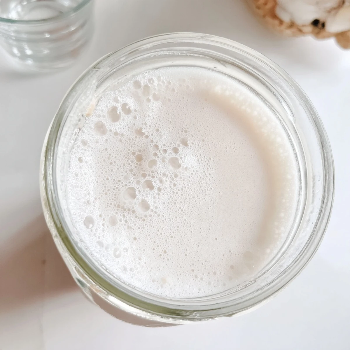 Creamy homemade almond milk poured into a clear glass jar with fresh almonds