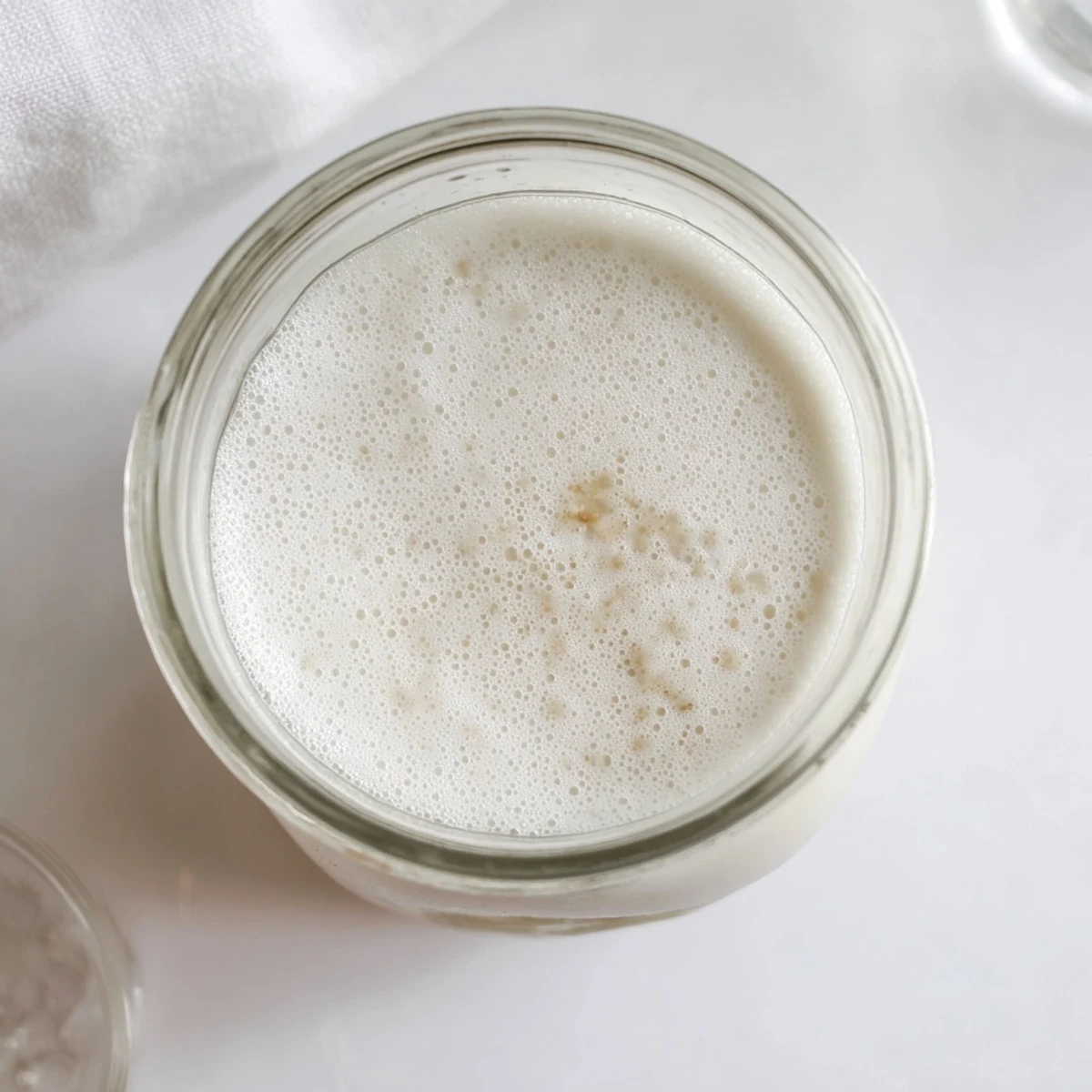 White frothy almond milk swirling in a blender pitcher with raw almond pieces