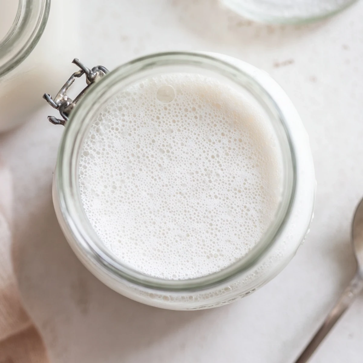 Glass of fresh almond milk on wooden table surrounded by raw almonds and vanilla pod