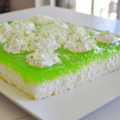 Lime poke cake soaked with gelatin and topped with whipped cream for a refreshing summer dessert.
