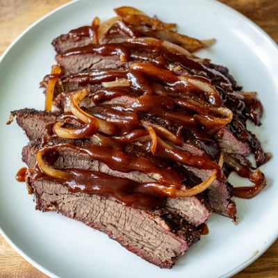 Tender Slow Cooked Beef Brisket with BBQ Sauce rests in a slow cooker pot, glistening with tangy, homemade sauce.